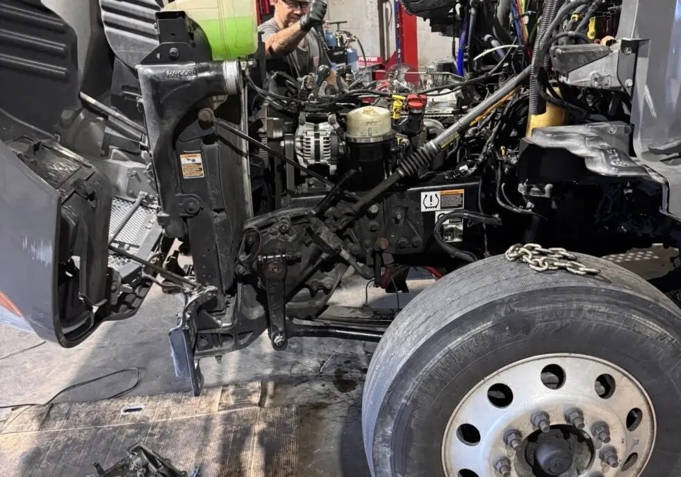 Truck Pit Stop mechanic working in the engine bay of a semi truck with the cylinder head on the floor